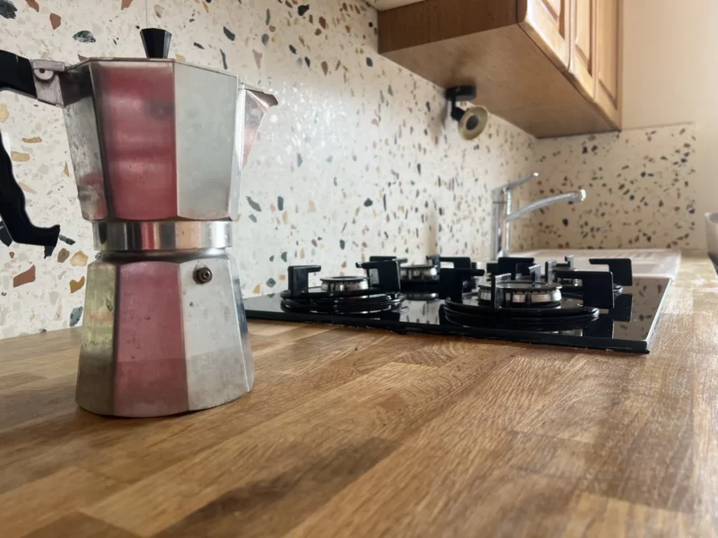 Gros plan sur une cafetière italienne posée sur le plan de travail en chêne d'une cuisine parisienne, crédence en terrazzo en arrière-plan